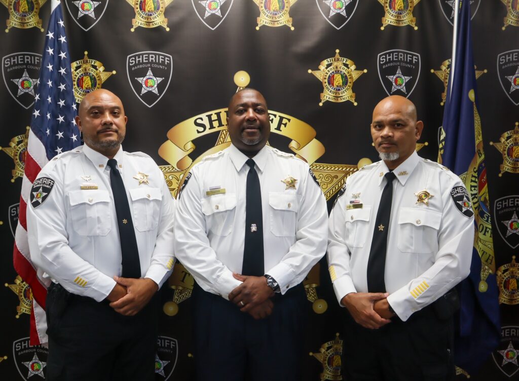 Three Barbour County Sheriff's Office leaders in white dress uniforms in front of the Sheriff's Office backdrop